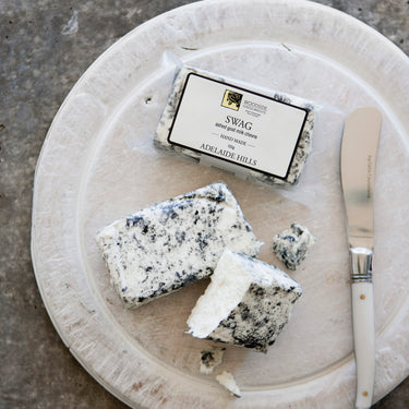 Swag Chèvre on black plate in packet and out of packet with knife, crumbling